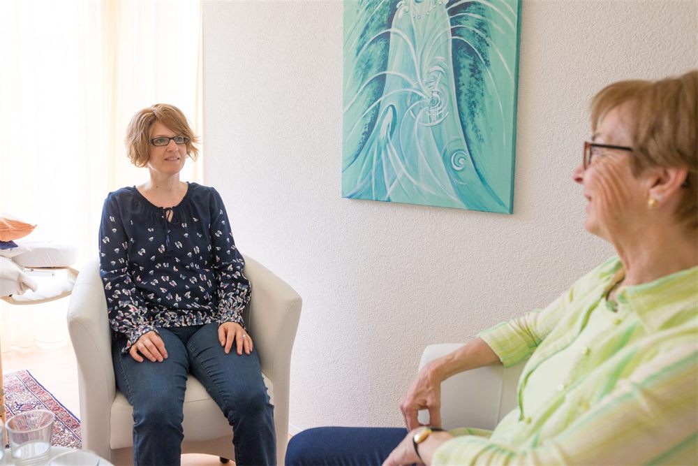 Zwei Frauen sitzen einander in Sesseln gegenüber und sprechen miteinander.