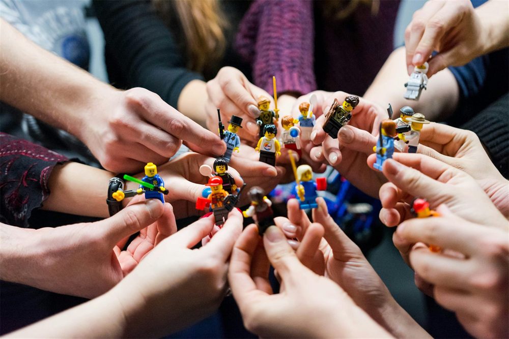 Mehrere Hände halten in einem Kreis LEGO-Figuren in die Mitte.